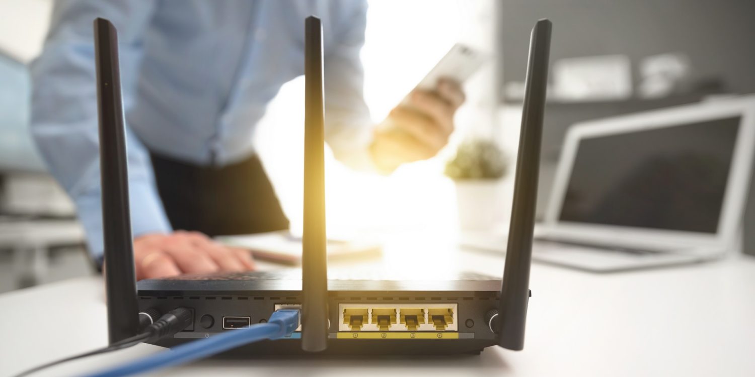 Wireless router with three antennas and cable connected. Man using smartphone in background